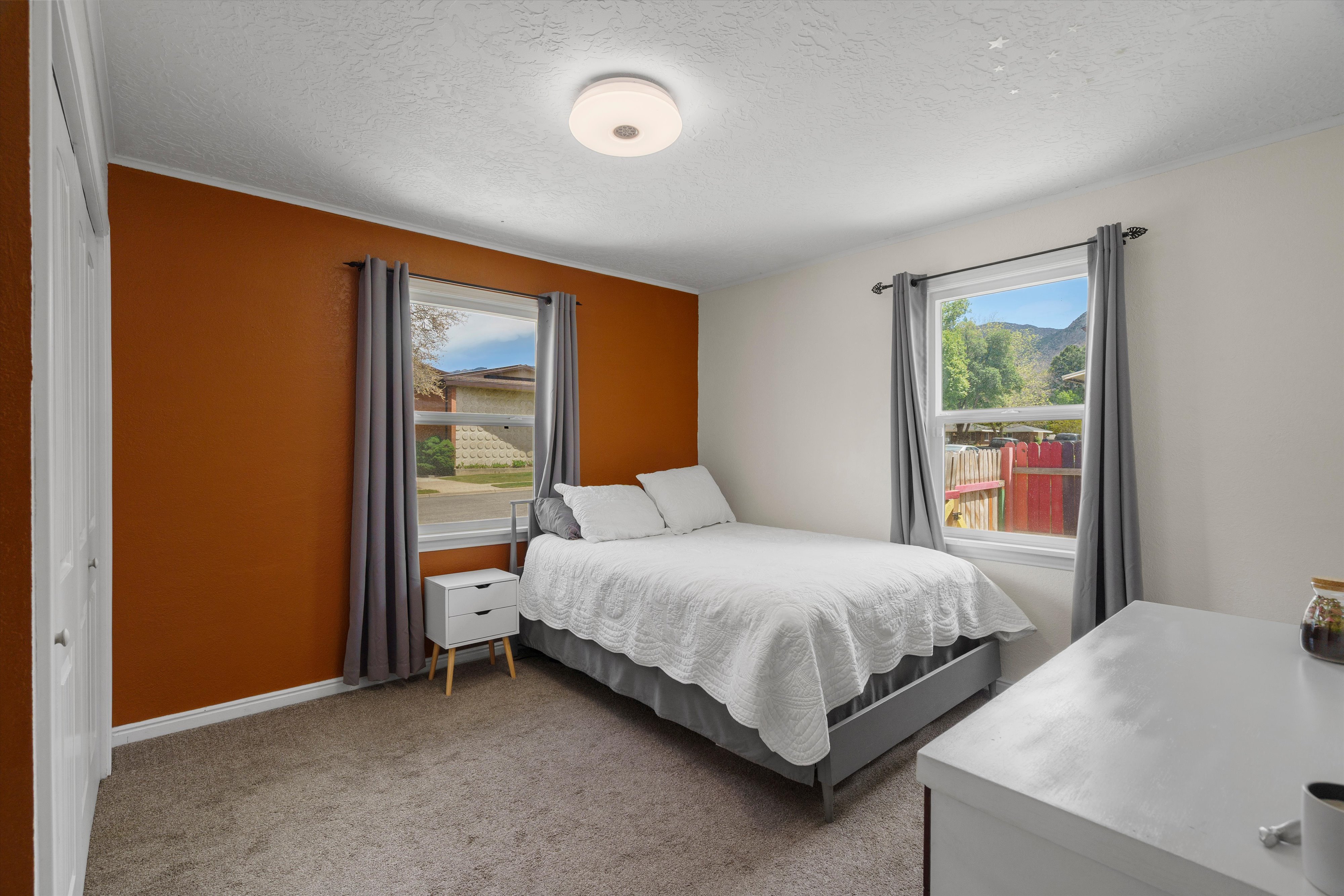 Carpeted bedroom featuring a textured ceiling, a flush mount light fixture, and two windows with mountain scenery