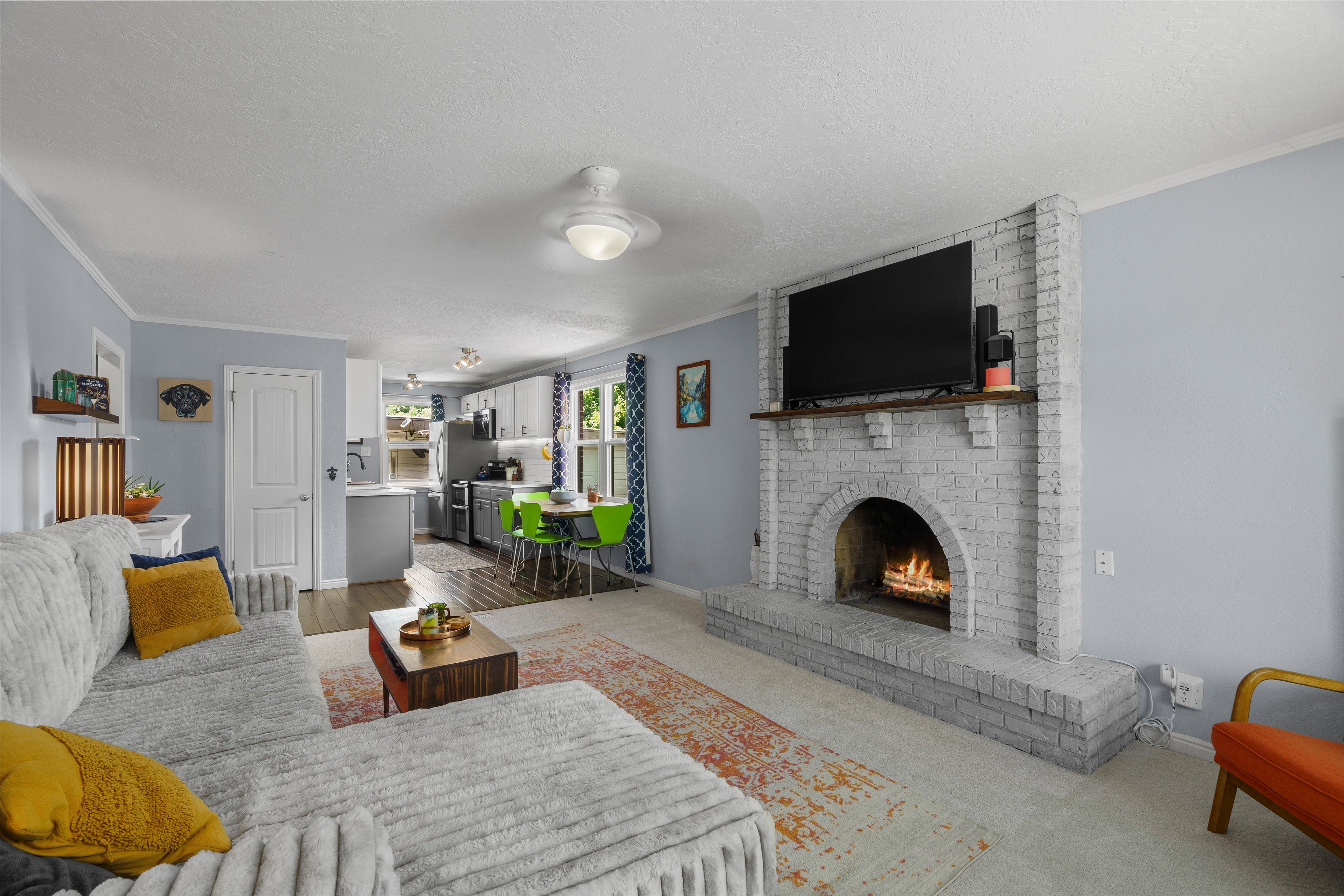 Living area featuring a painted brick fireplace with a wood mantle, light blue walls, and a ceiling fan