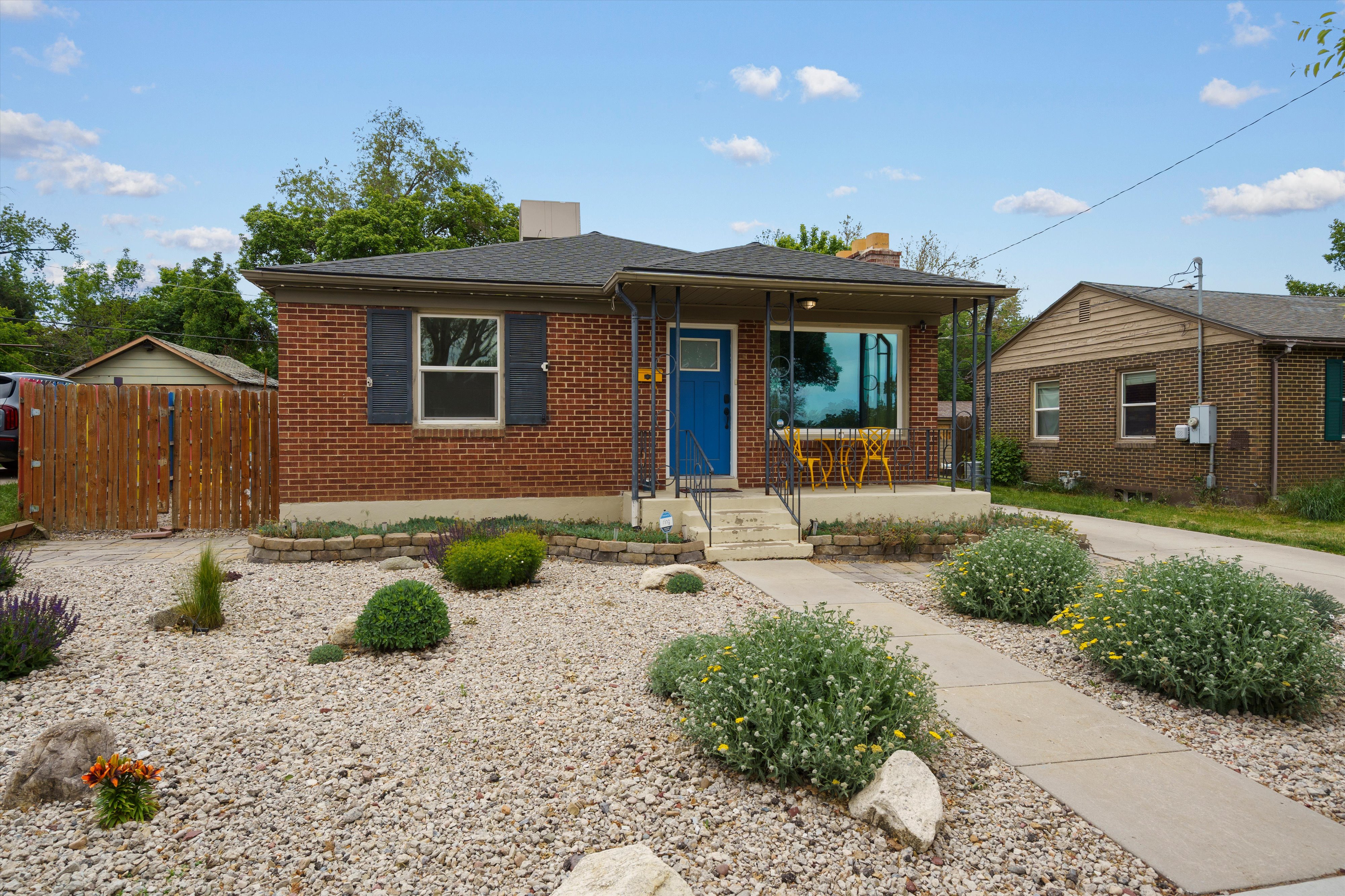 Brick exterior featuring a covered front porch with iron railings, a vibrant blue entry door, and dark window shutters