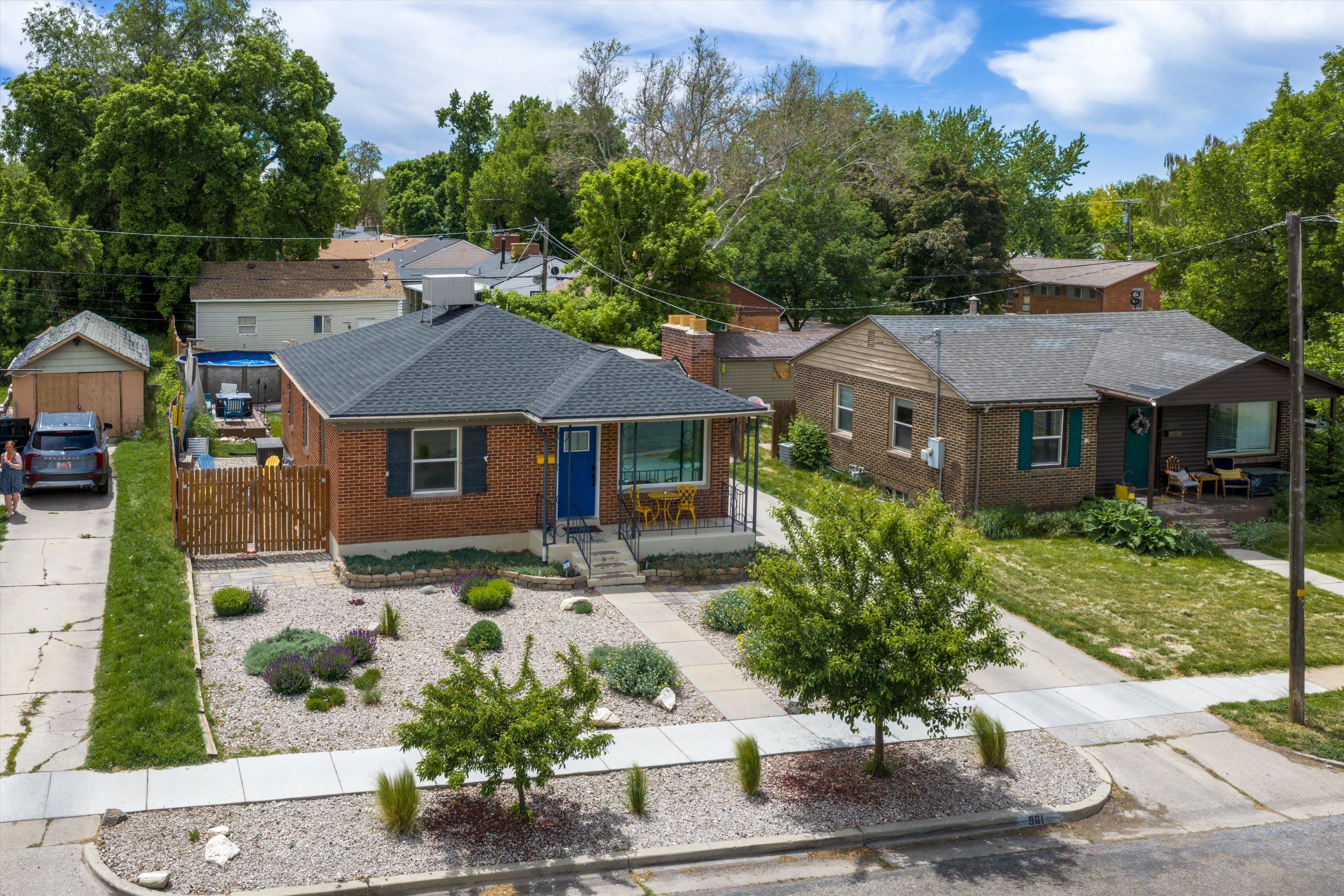 Brick facade home featuring a contrasting blue entry door, dark roof shingles, and a front yard with gravel landscaping