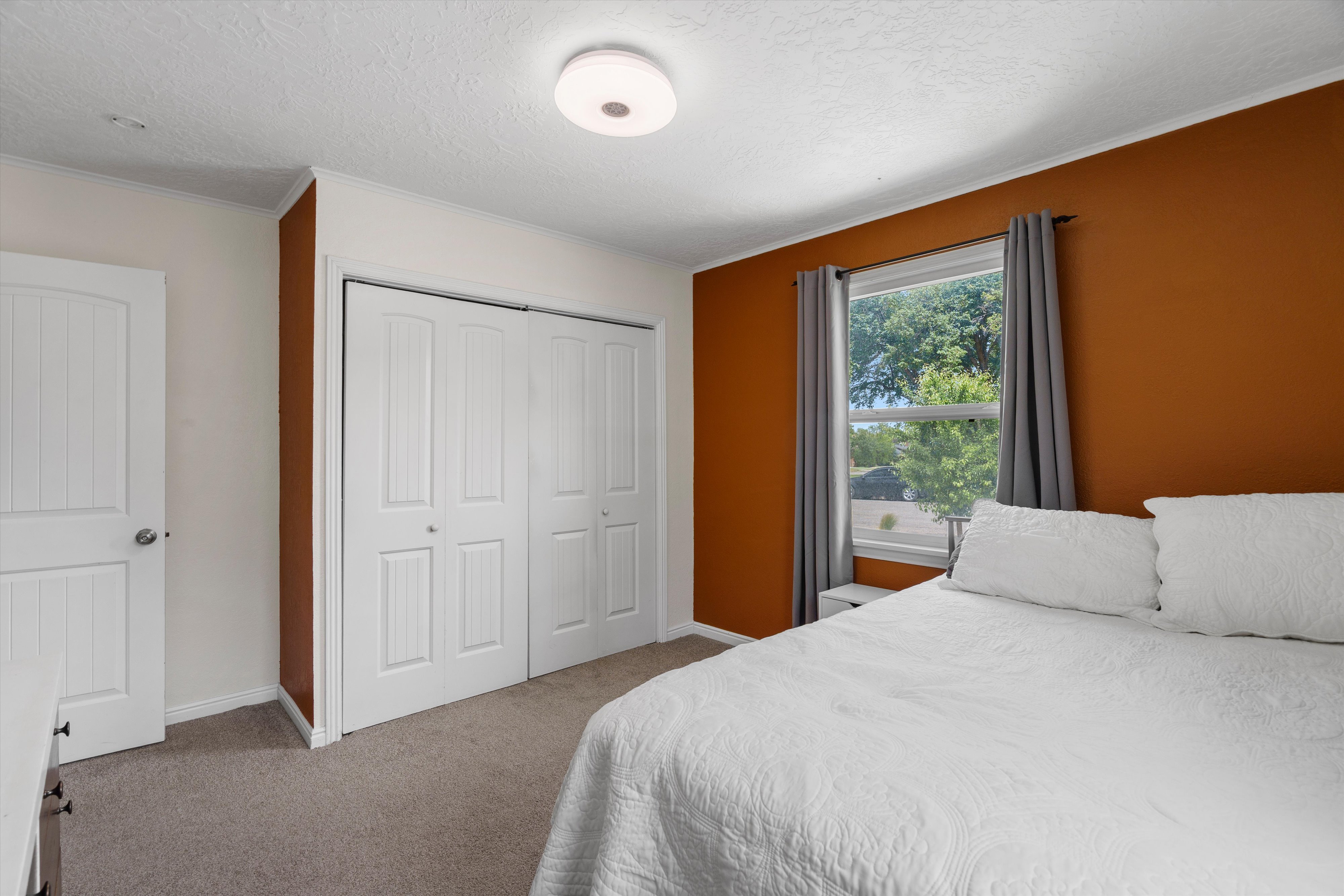 Wall-to-wall carpeting in a neutral tone, featuring a window with a treed backdrop