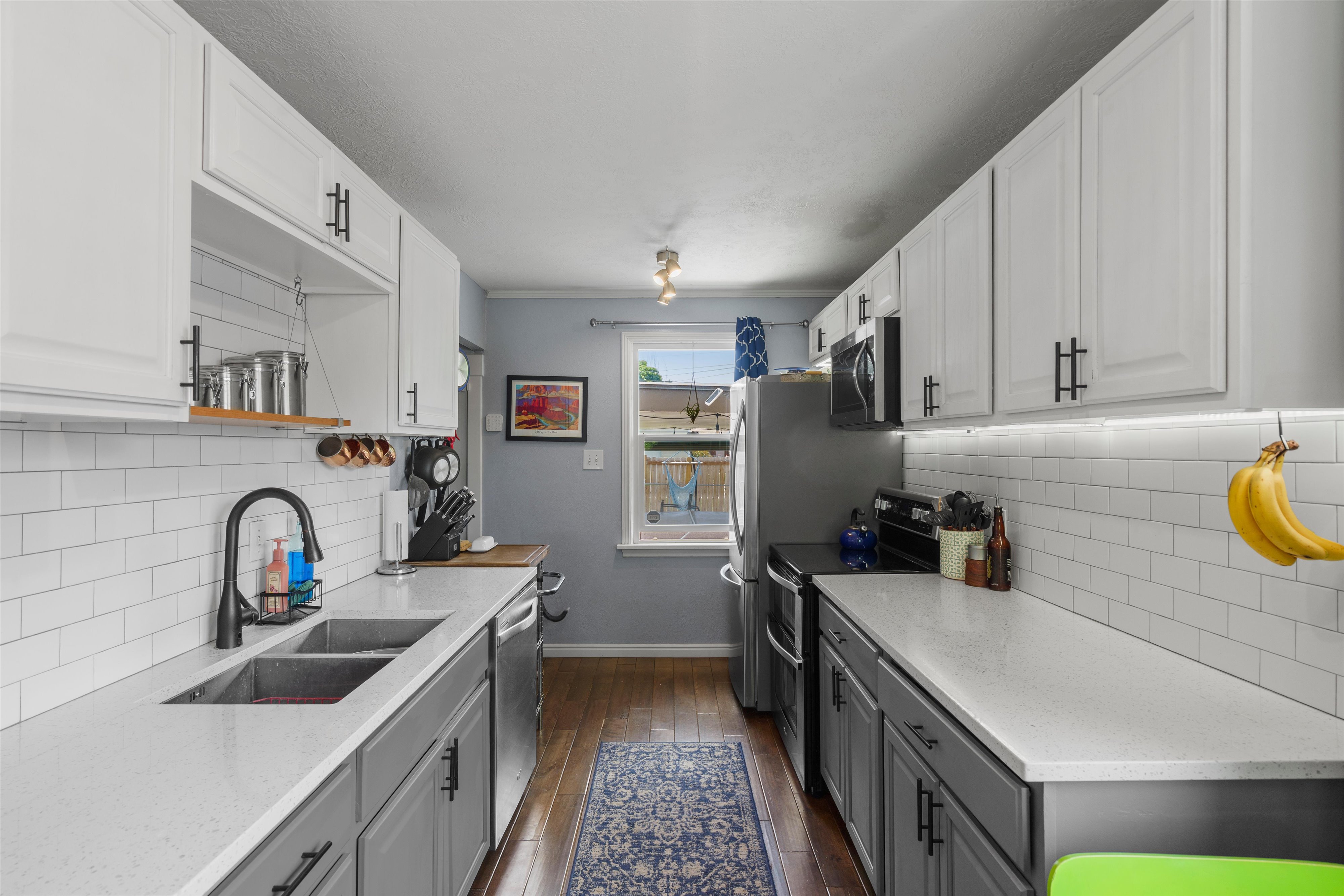 Galley kitchen featuring dual-toned cabinetry, subway tile backsplash, stainless steel appliances, and wood-finish flooring
