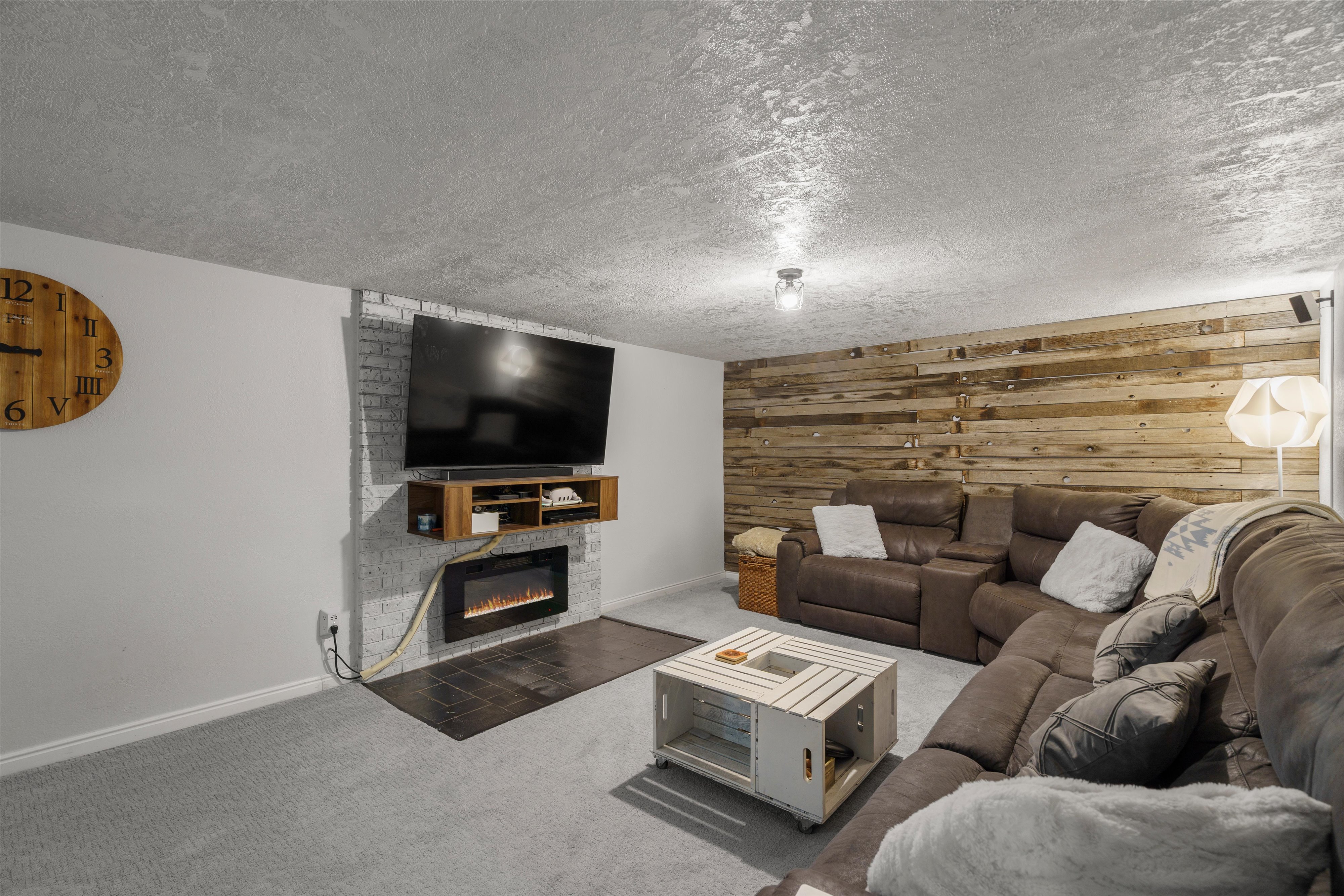 Recreational area featuring an accent wall with a mounted electric fireplace, a wall-mounted media console, and a wood-finish plank accent wall