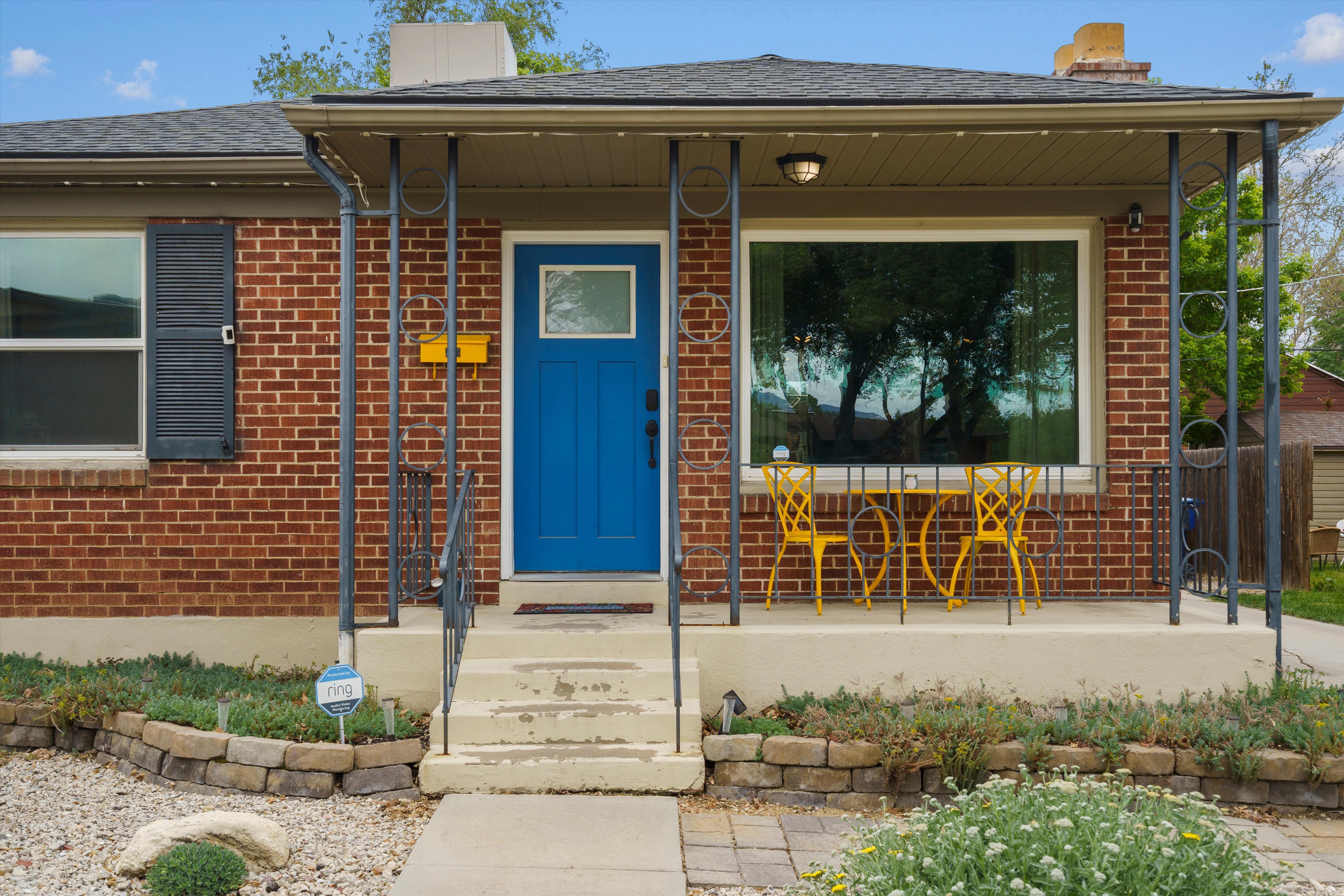 Brick exterior featuring a covered porch with decorative metal supports, an accent blue entry door, and a large front picture window