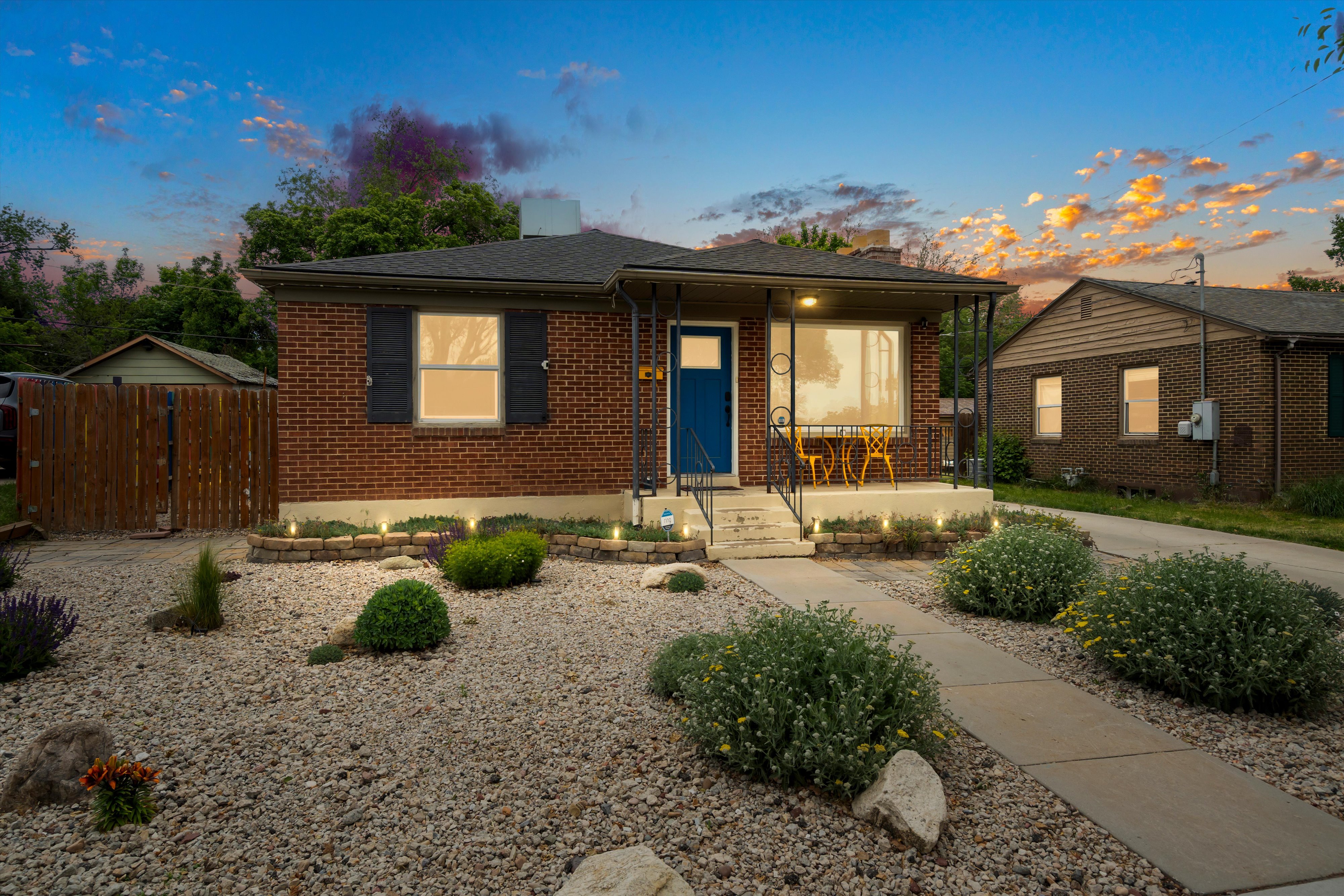Brick home with a covered front porch and a distinctive blue entry door. Low maintenance xeriscape front yard.