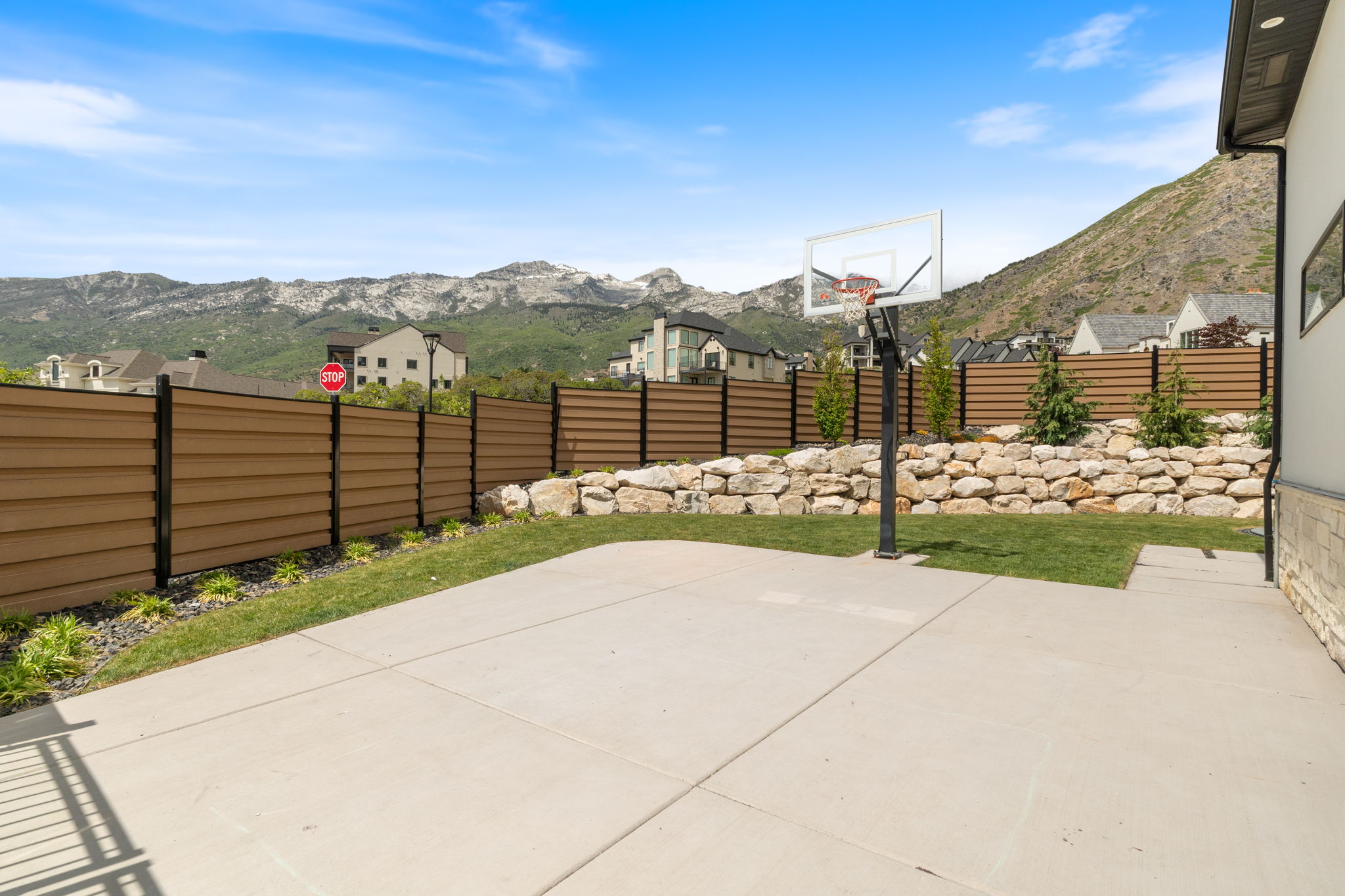 Expansive concrete patio with integrated basketball hoop and a retaining wall featuring natural stone