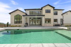 Contemporary residence featuring a rectangular swimming pool, expansive concrete patio, light-toned stone and stucco exterior, large black-framed windows, and a covered patio area