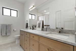 Double vanity featuring light wood cabinetry with gold-tone hardware, a light stone countertop, and two integrated rectangular sinks with modern chrome faucets
