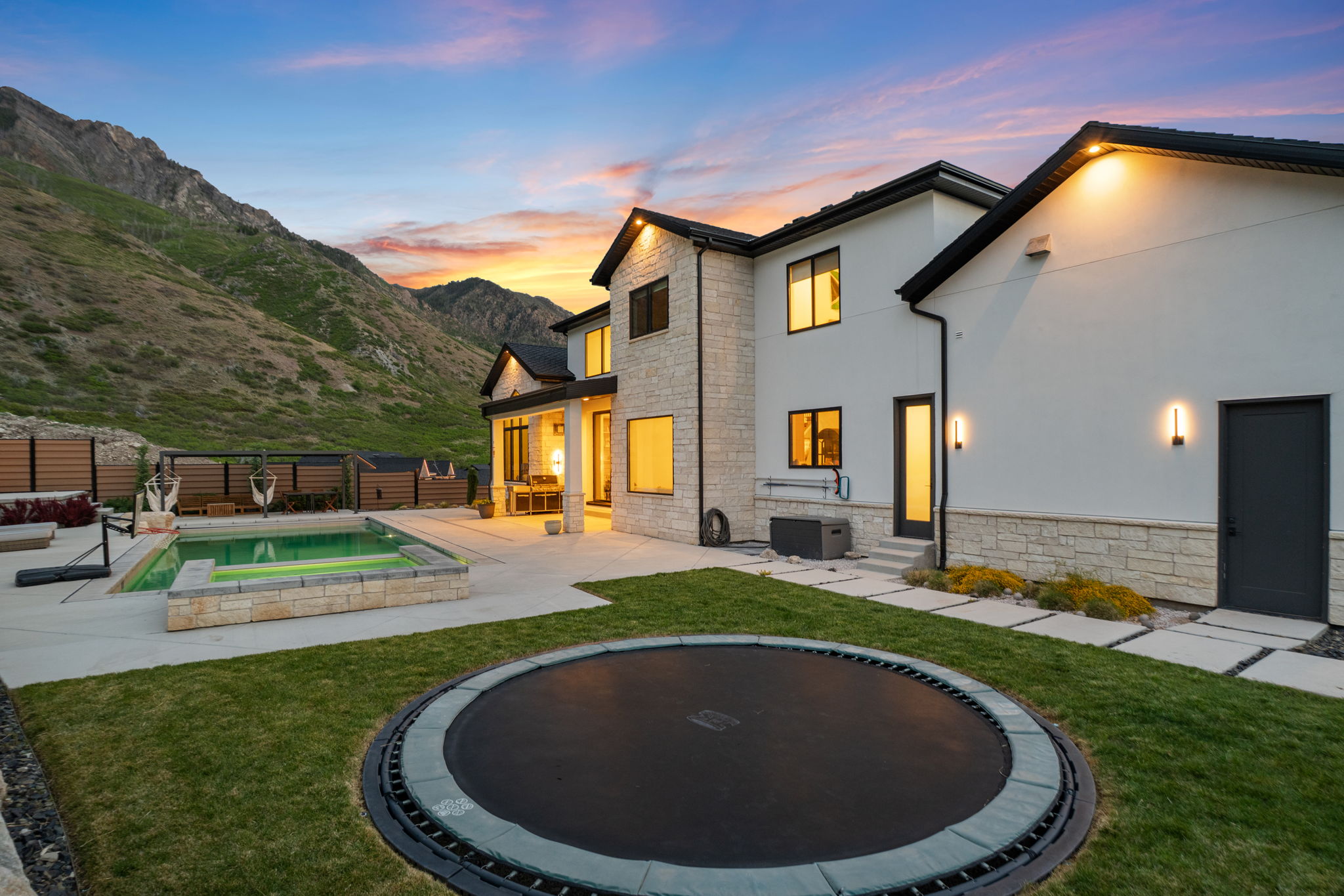 Expansive backyard featuring a built-in trampoline, concrete patio, and a swimming pool with integrated spa