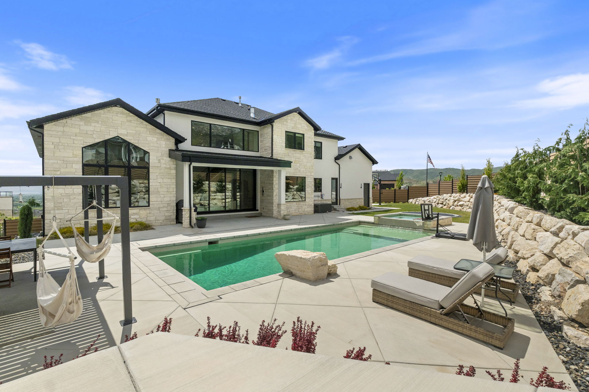 Expansive outdoor living area featuring a rectangular swimming pool with a connected hot tub