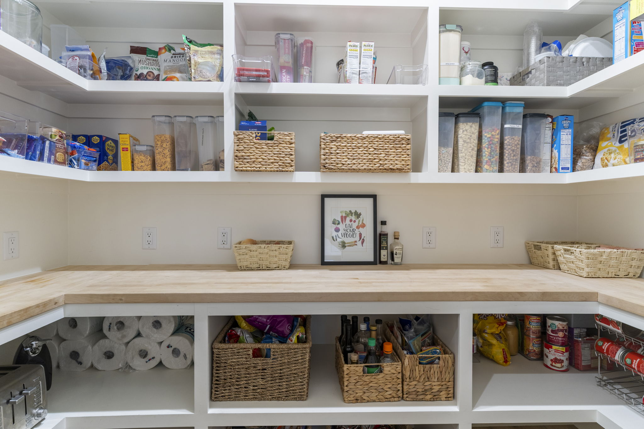 Dedicated pantry featuring extensive open shelving, wrap-around wood-finish countertops, built-in lower storage compartments, and multiple electrical outlets