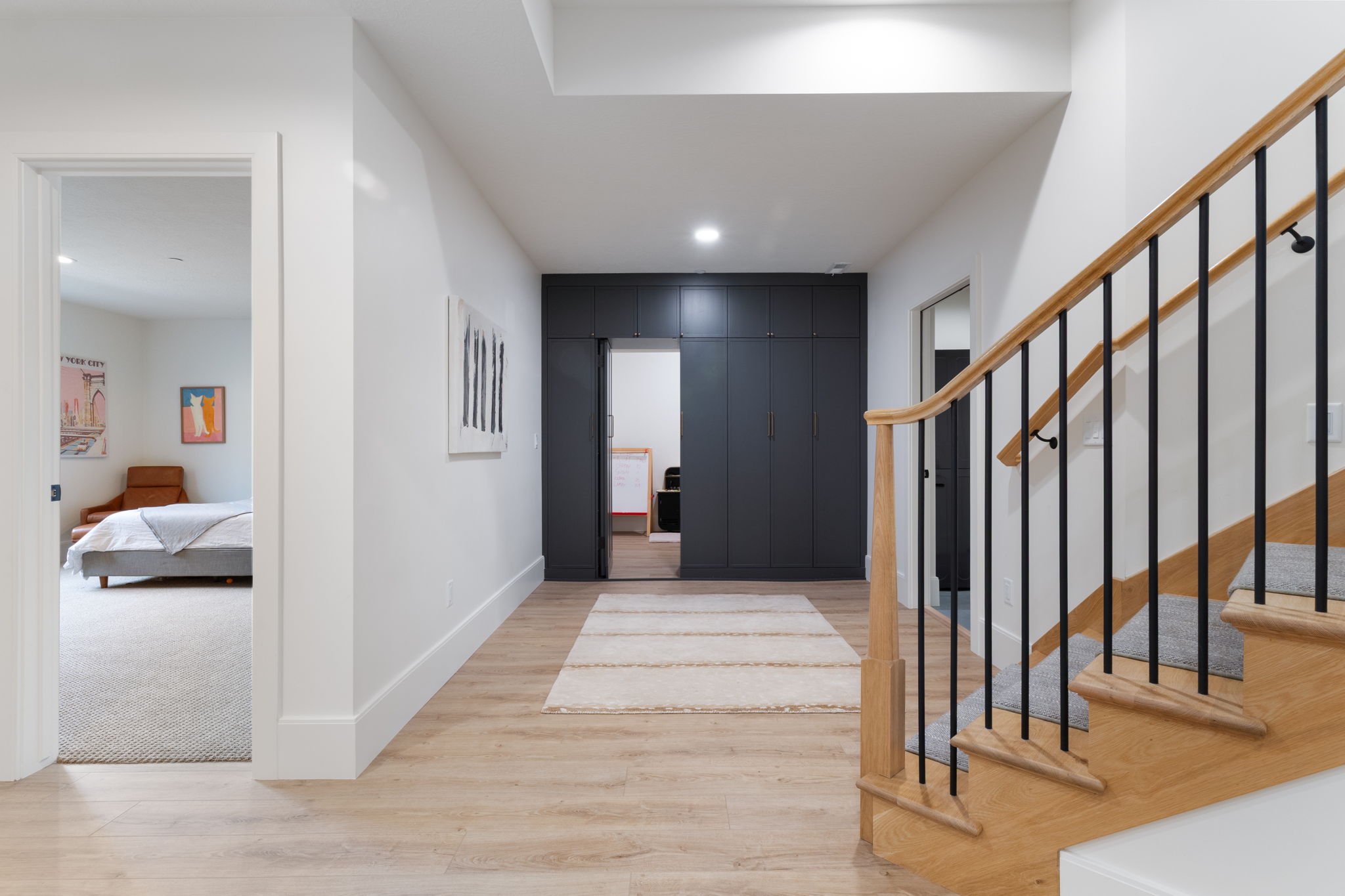 Hallway featuring wood-finish flooring, a light wood staircase with black metal balusters, and recessed lighting