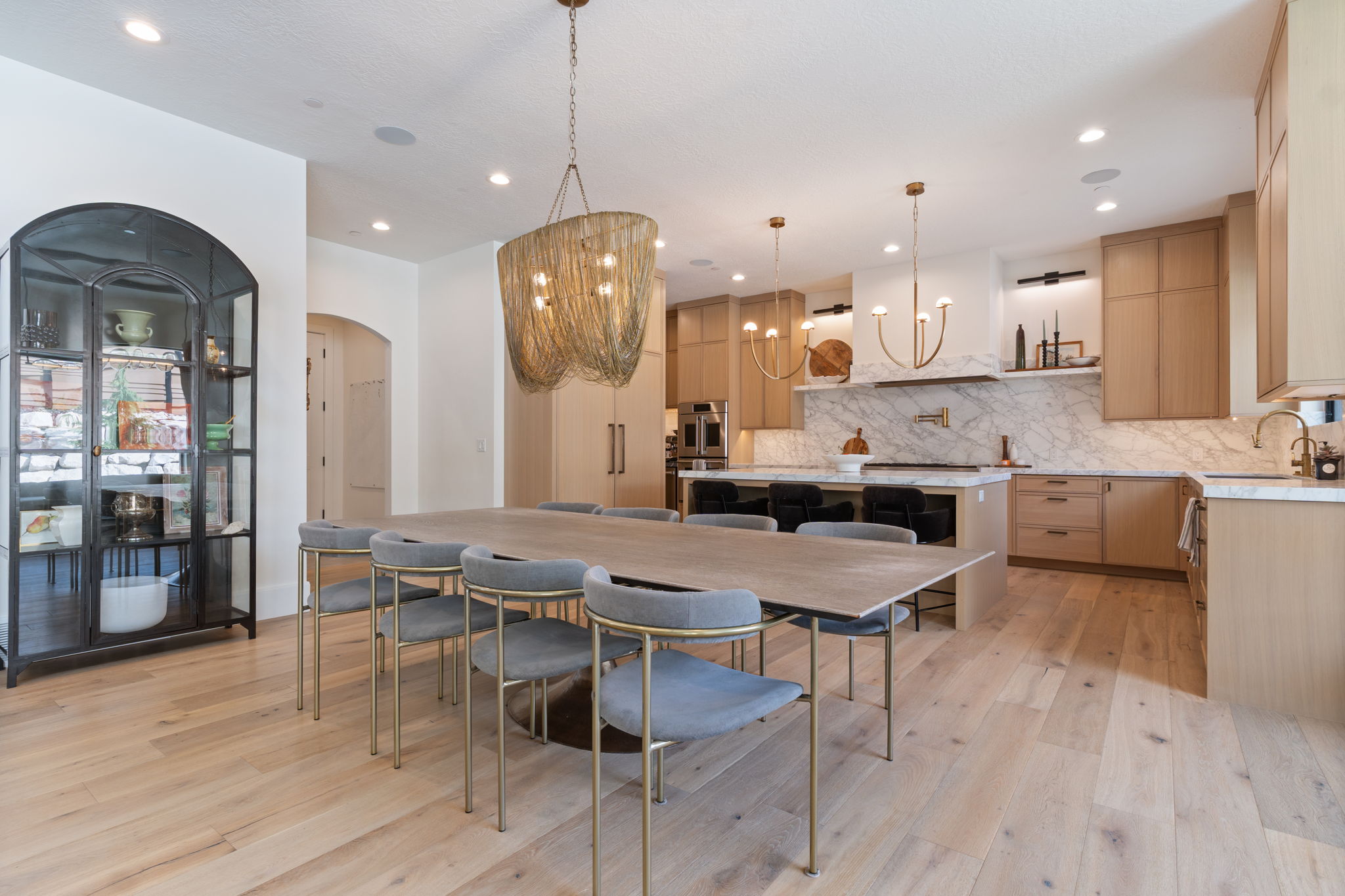 Open-concept dining area with wood-finish flooring, a large island with seating, white oak wood cabinetry, and integrated appliances