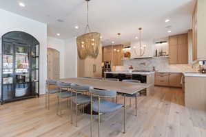 Open-concept dining area with wood-finish flooring, a large island with seating, white oak wood cabinetry, and integrated appliances