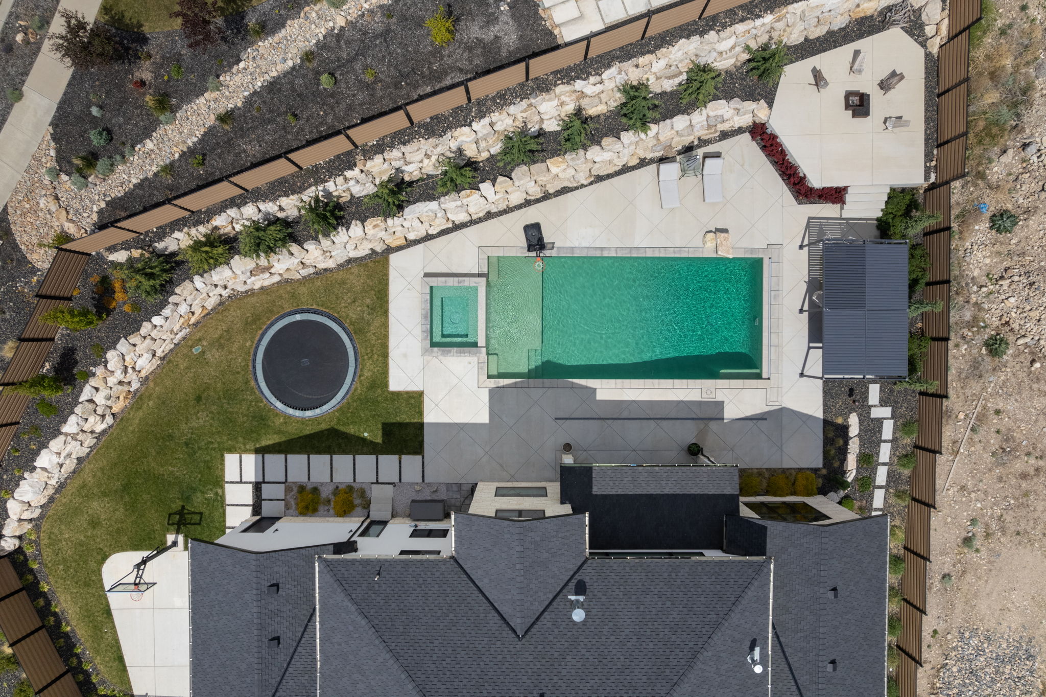 Expansive backyard featuring a rectangular swimming pool with an integrated spa, extensive concrete patio, and a dedicated fire pit area