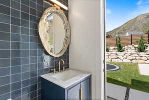 Pool bathroom vanity with a white countertop and gold-toned faucet, featuring a unique mirror and dark tiled wall