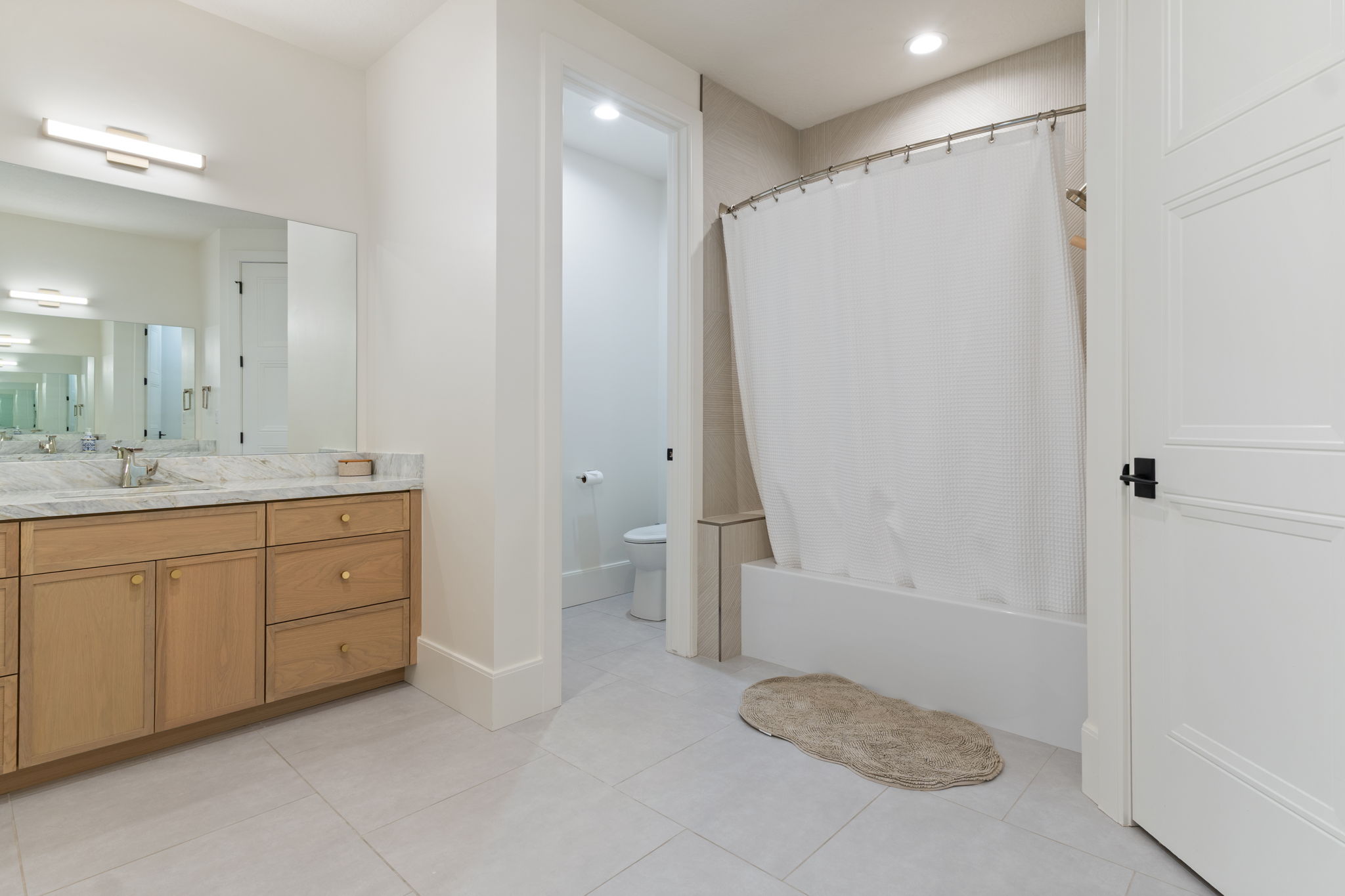 Bathroom featuring a light wood-finish vanity with a stone countertop, an integrated sink, and a large mirror