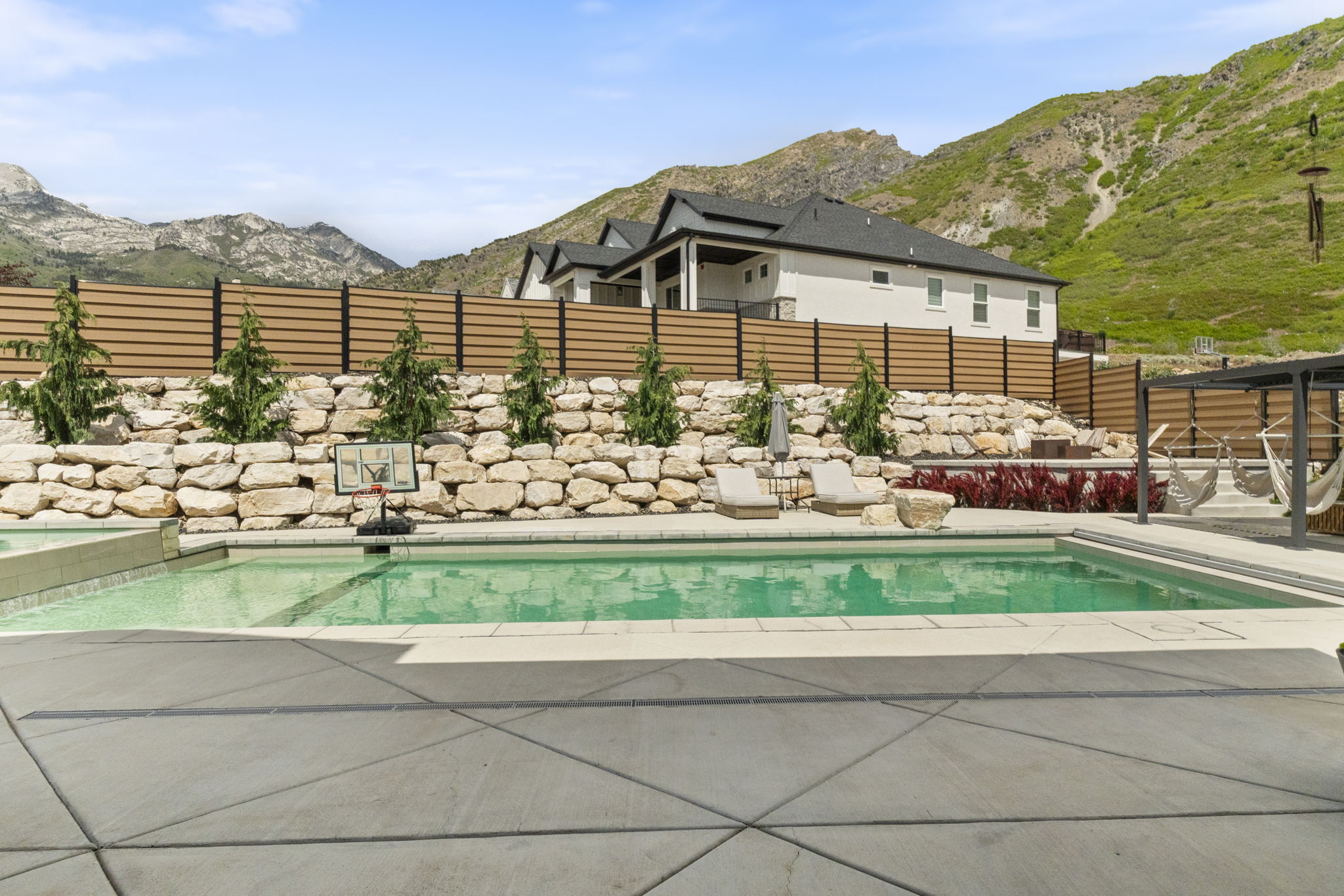 Outdoor swimming pool with integrated spa, surrounded by extensive concrete patio and a stone retaining wall
