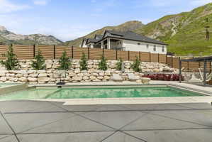 Outdoor swimming pool with integrated spa, surrounded by extensive concrete patio and a stone retaining wall
