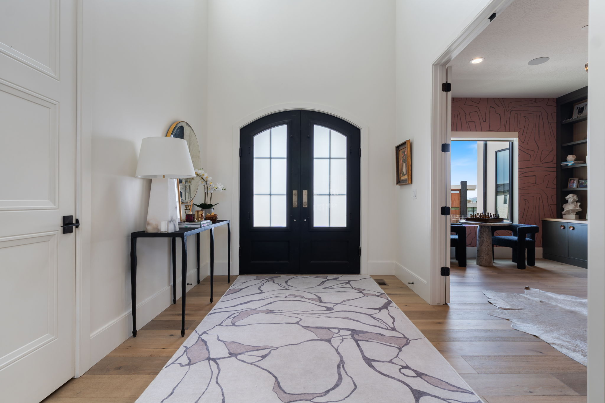Grand entryway featuring an arched double door with glass panels, light wood-finish flooring, and high ceilings