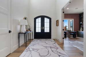 Grand entryway featuring an arched double door with glass panels, light wood-finish flooring, and high ceilings