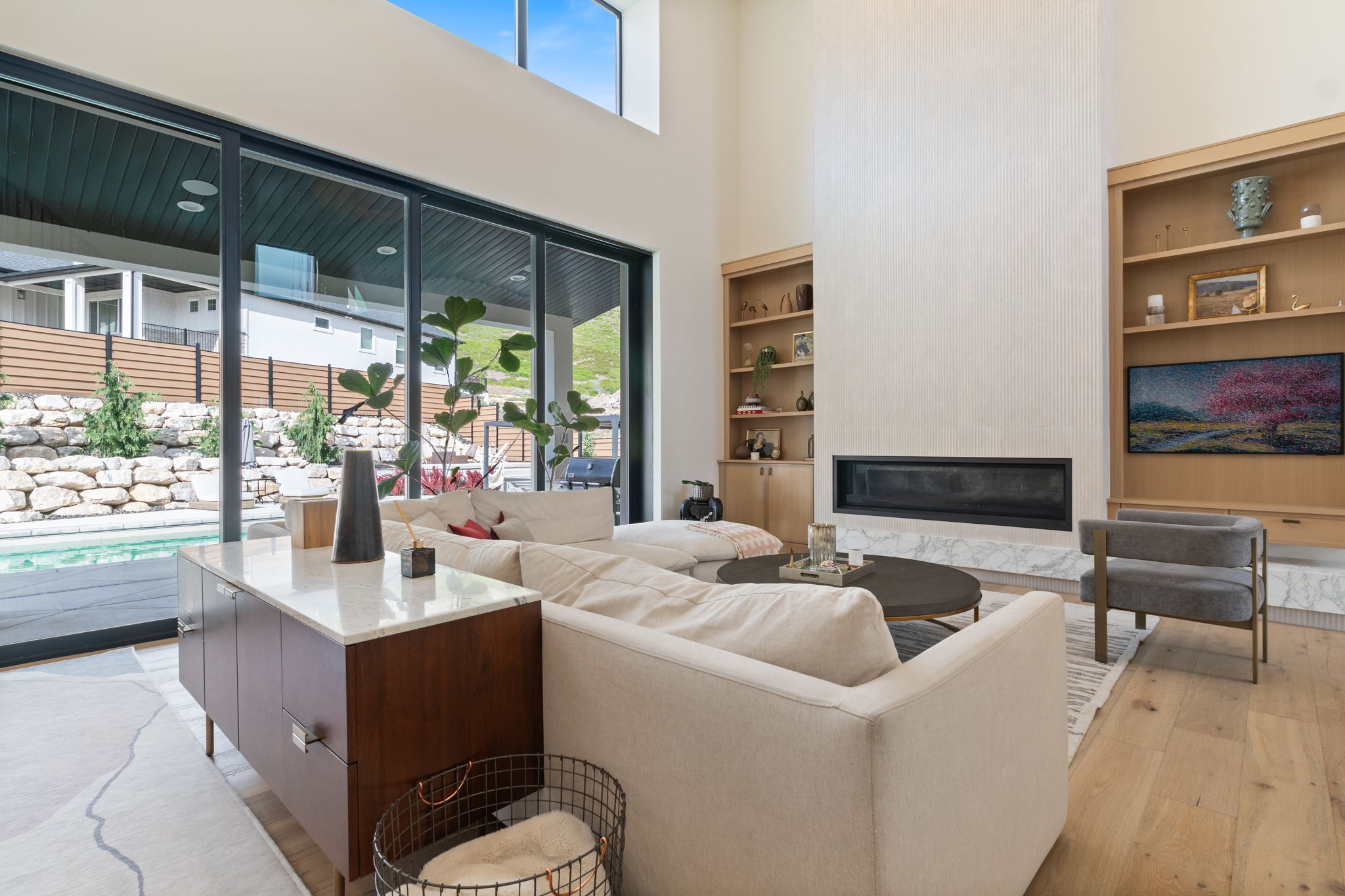 Spacious living area featuring a linear fireplace, built-in shelving, wood-finish flooring, and large sliding glass doors opening to an outdoor pool