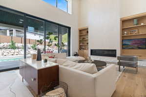 Spacious living area featuring a linear fireplace, built-in shelving, wood-finish flooring, and large sliding glass doors opening to an outdoor pool