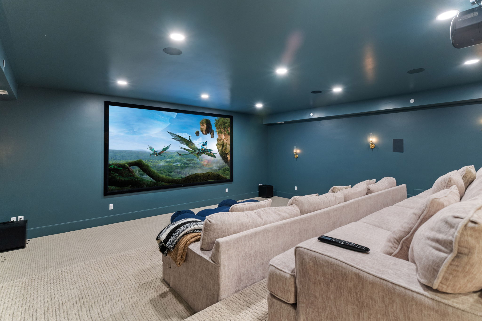 Dedicated media room featuring a large projection screen, recessed lighting, and wall-mounted sconces