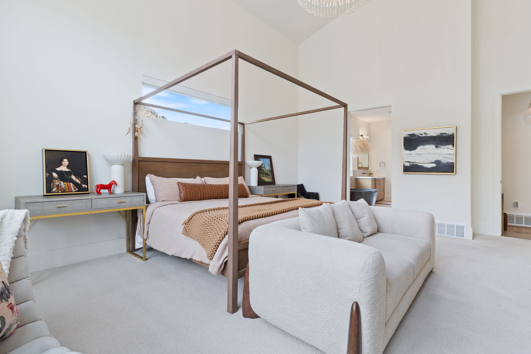 Vaulted ceilings highlight this expansive bedroom featuring a four-poster bed frame, neutral-toned carpeting, and high windows providing natural illumination