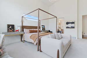 Vaulted ceilings highlight this expansive bedroom featuring a four-poster bed frame, neutral-toned carpeting, and high windows providing natural illumination