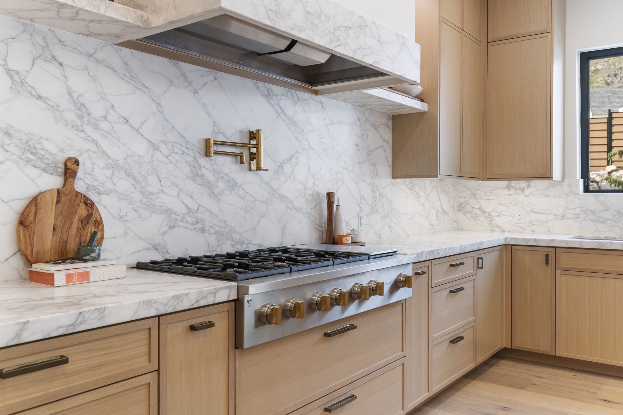 Stainless steel range with a pot filler faucet, marble slab backsplash and countertops, with white oak cabinetry