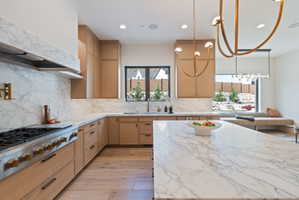 Spacious kitchen featuring an expansive island, white oak cabinetry, integrated stainless steel appliances, and premium marble countertops and backsplash