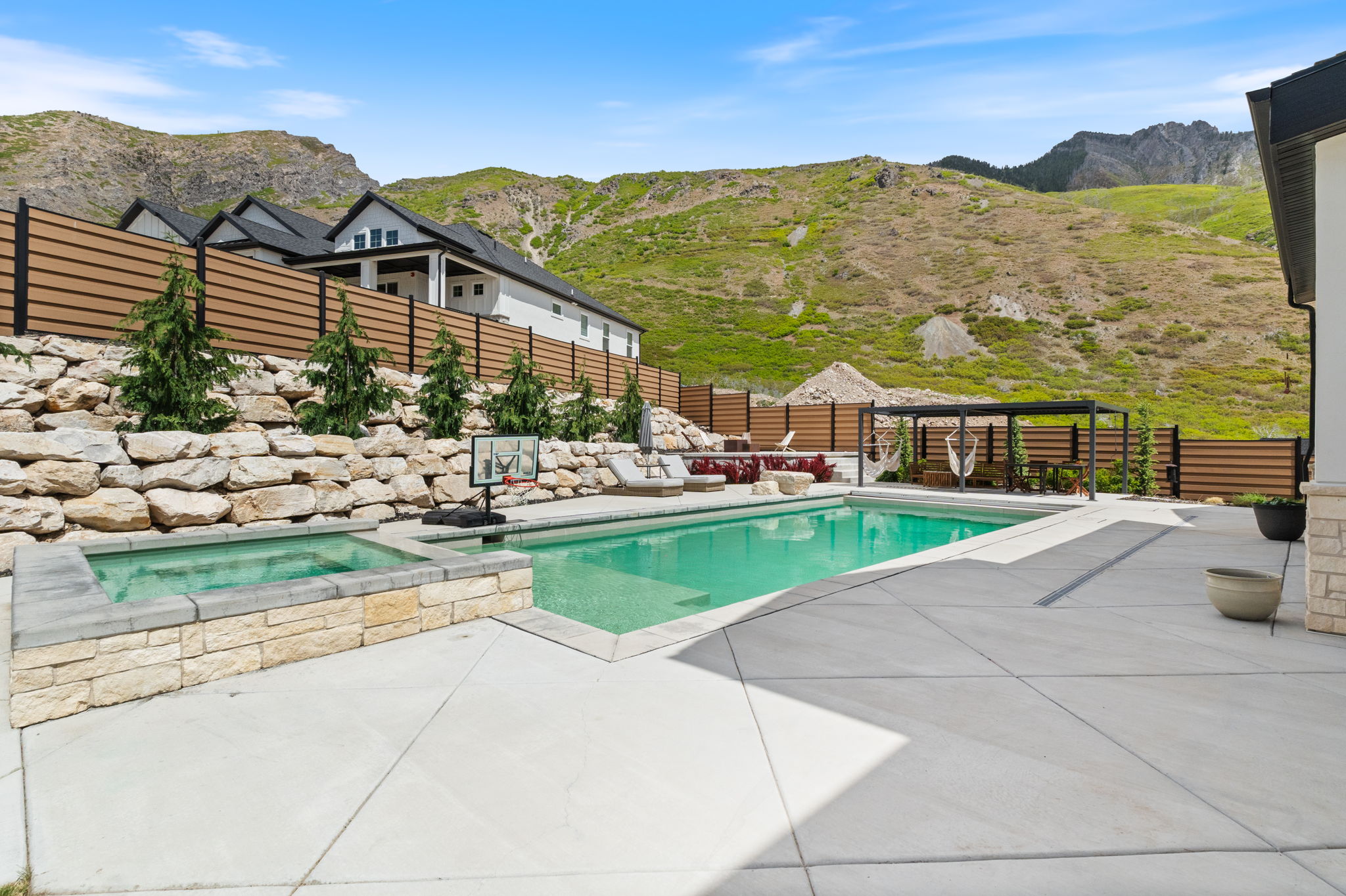 Outdoor entertaining area featuring a swimming pool, integrated hot tub with stone surround, and extensive concrete patio