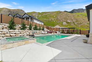 Outdoor entertaining area featuring a swimming pool, integrated hot tub with stone surround, and extensive concrete patio