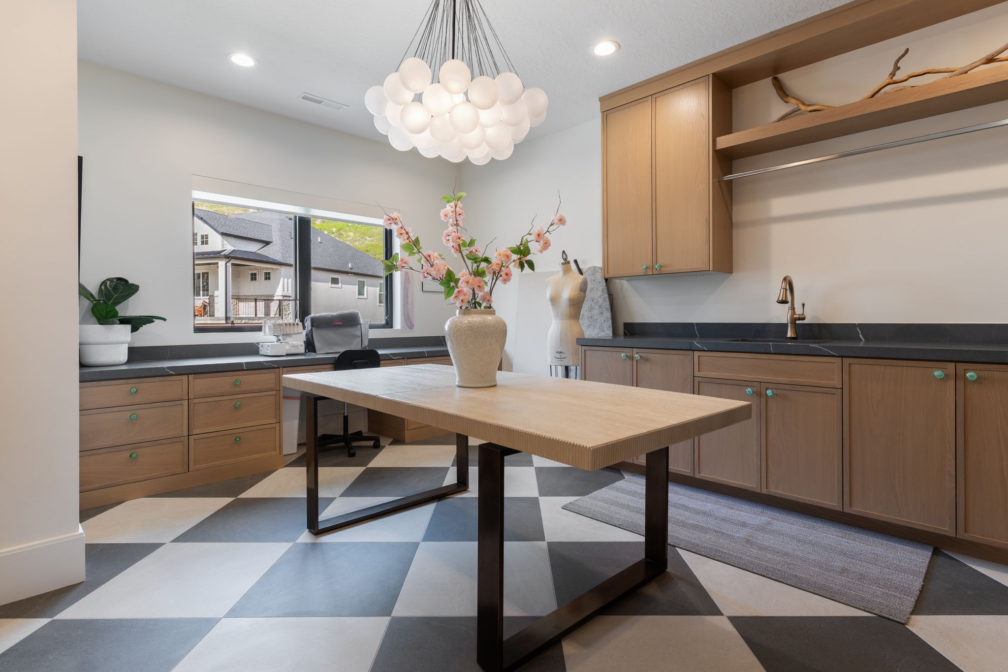 Spacious utility room featuring checkerboard flooring, natural wood-finish cabinetry, dark countertops, an integrated sink with a bronze-finish faucet, and a large window