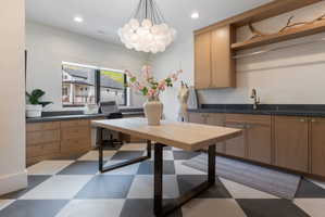 Spacious utility room featuring checkerboard flooring, natural wood-finish cabinetry, dark countertops, an integrated sink with a bronze-finish faucet, and a large window