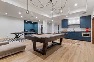 Spacious recreational area featuring wood-finish flooring, recessed lighting, and a modern chandelier