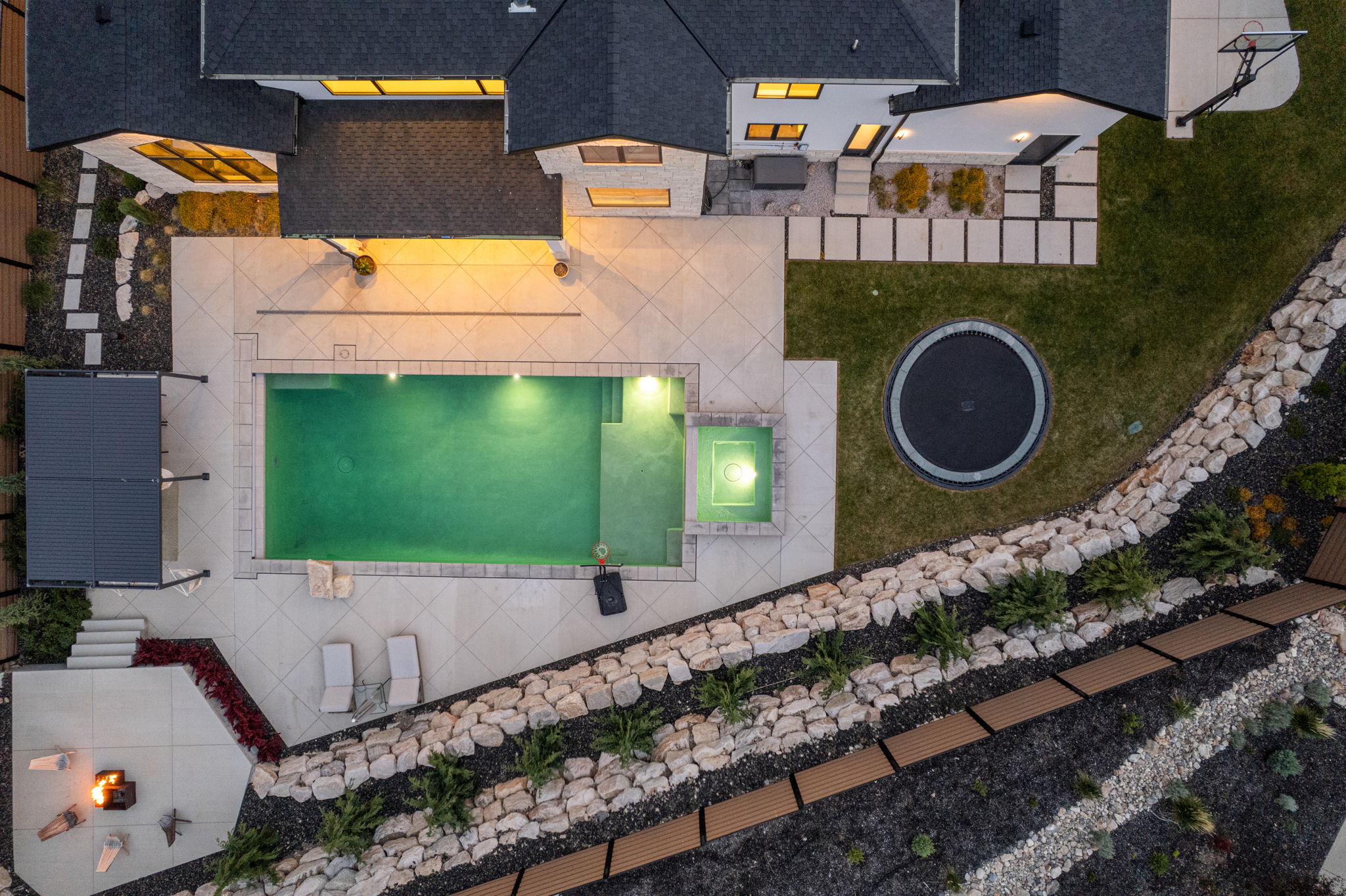 Expansive outdoor living area featuring a rectangular swimming pool with integrated spa, a paved patio, and a dedicated fire pit area