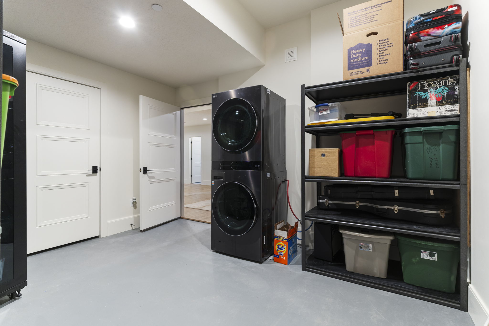 Laundry area featuring a stacked washer and dryer unit, light gray flooring, recessed lighting, and white paneled doors with black hardware