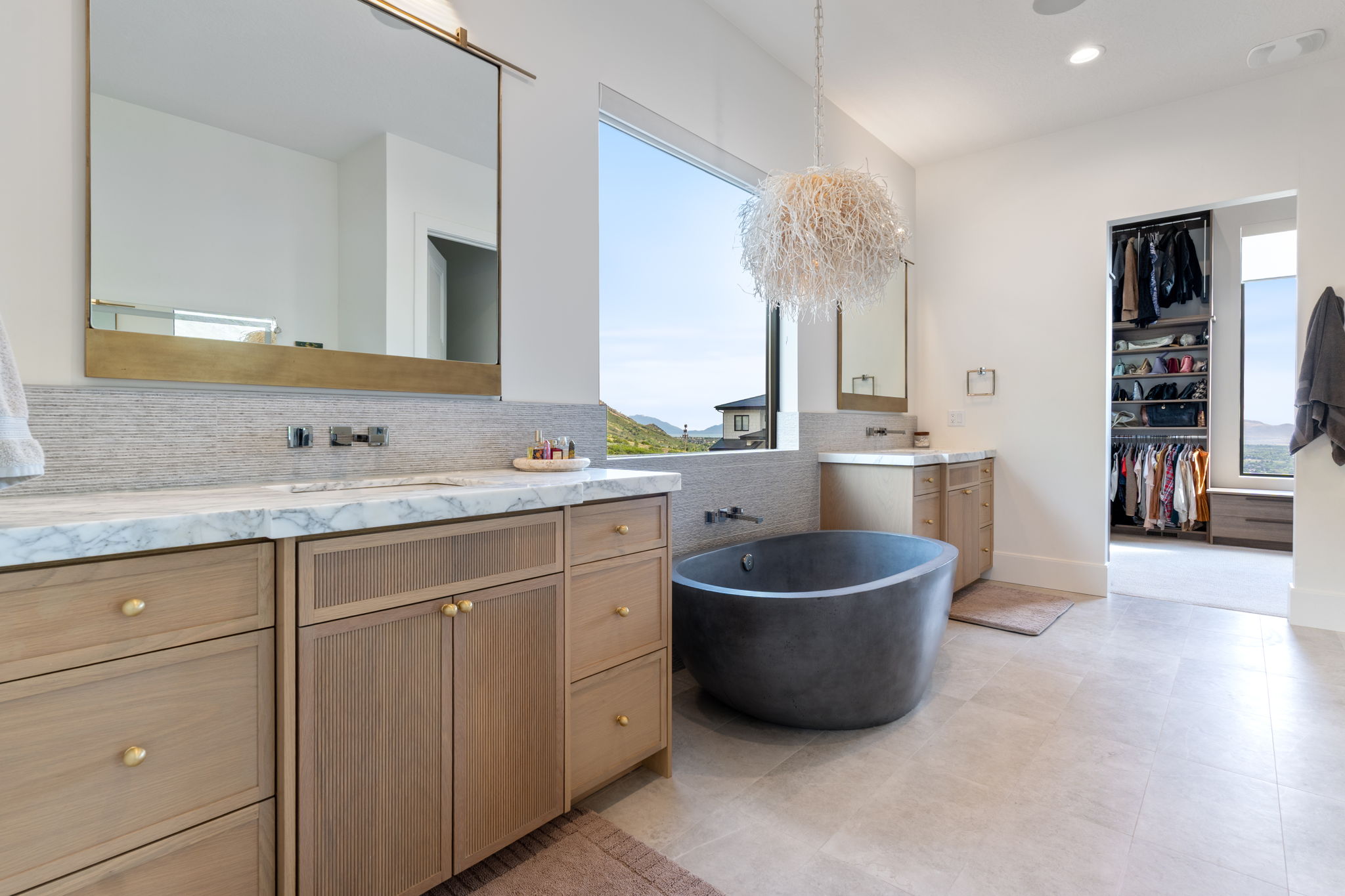 Contemporary bathroom featuring a freestanding soaking tub, dual vanity with light wood cabinetry, marble-finish countertop, and large format floor tiling