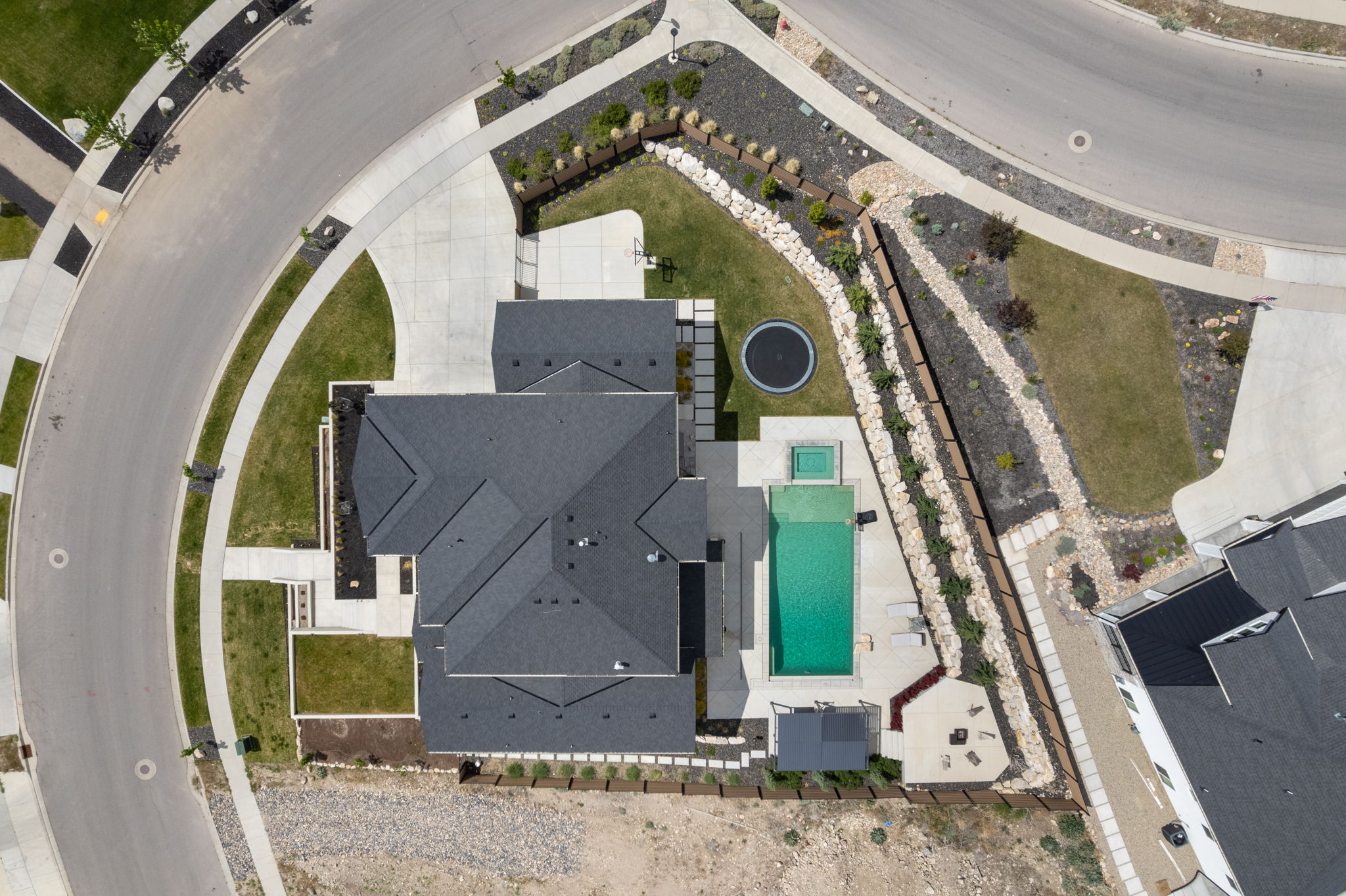 Expansive property featuring a dark shingle roof, a large rectangular pool with an attached spa, and extensive concrete patios