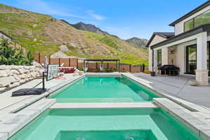 Expansive outdoor living area featuring a rectangular pool with an integrated spa, concrete patio, and stacked stone retaining wall
