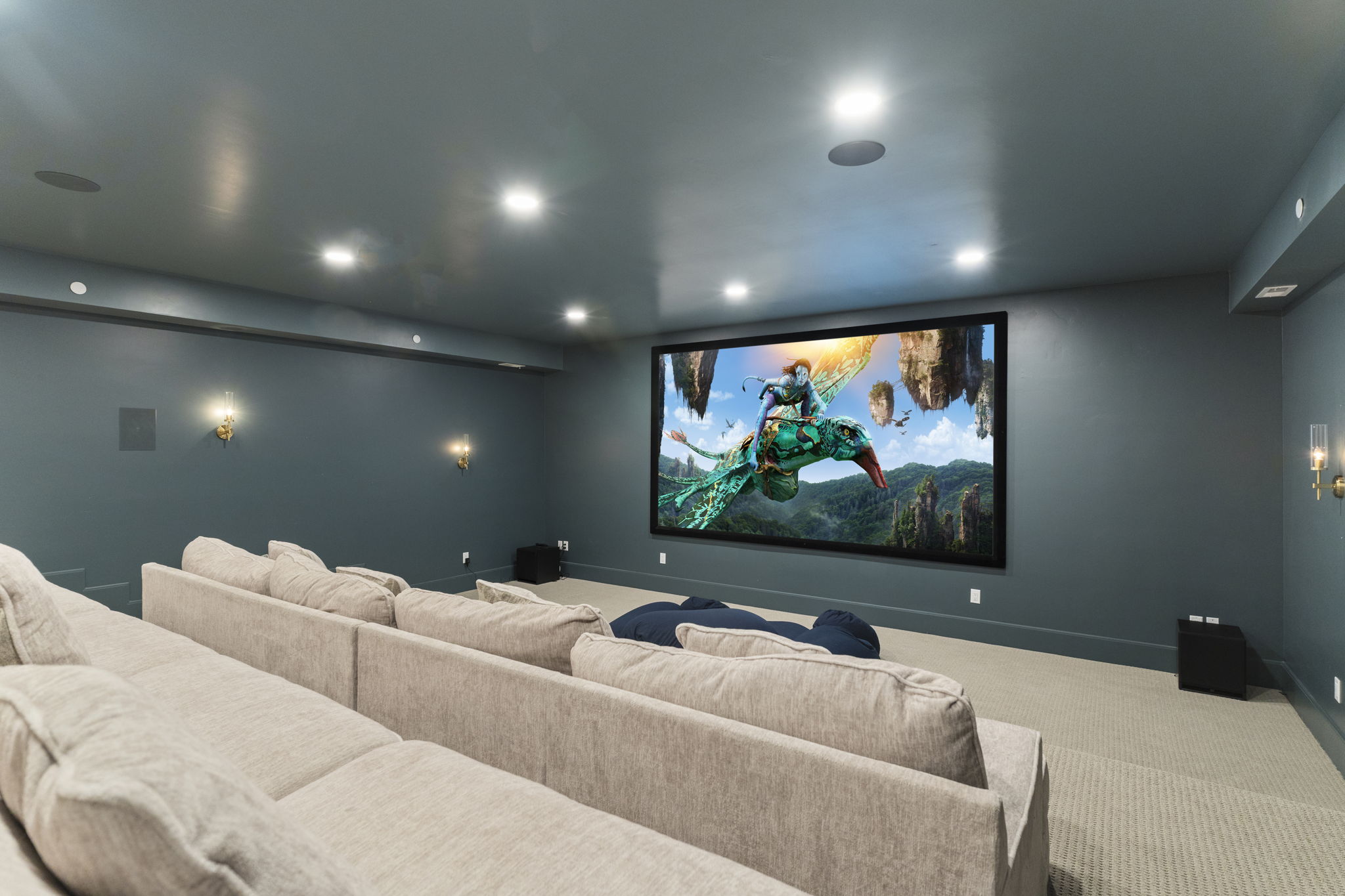Dedicated media room featuring a large projection screen, recessed ceiling lighting, and wall-mounted sconces