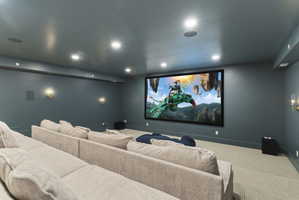 Dedicated media room featuring a large projection screen, recessed ceiling lighting, and wall-mounted sconces