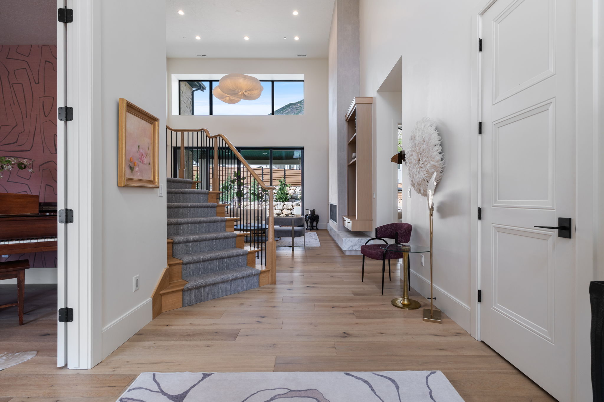 Grand entryway featuring wood-finish flooring, a carpeted staircase with wood handrails and black metal balusters, and a paneled white door with matte black hardware