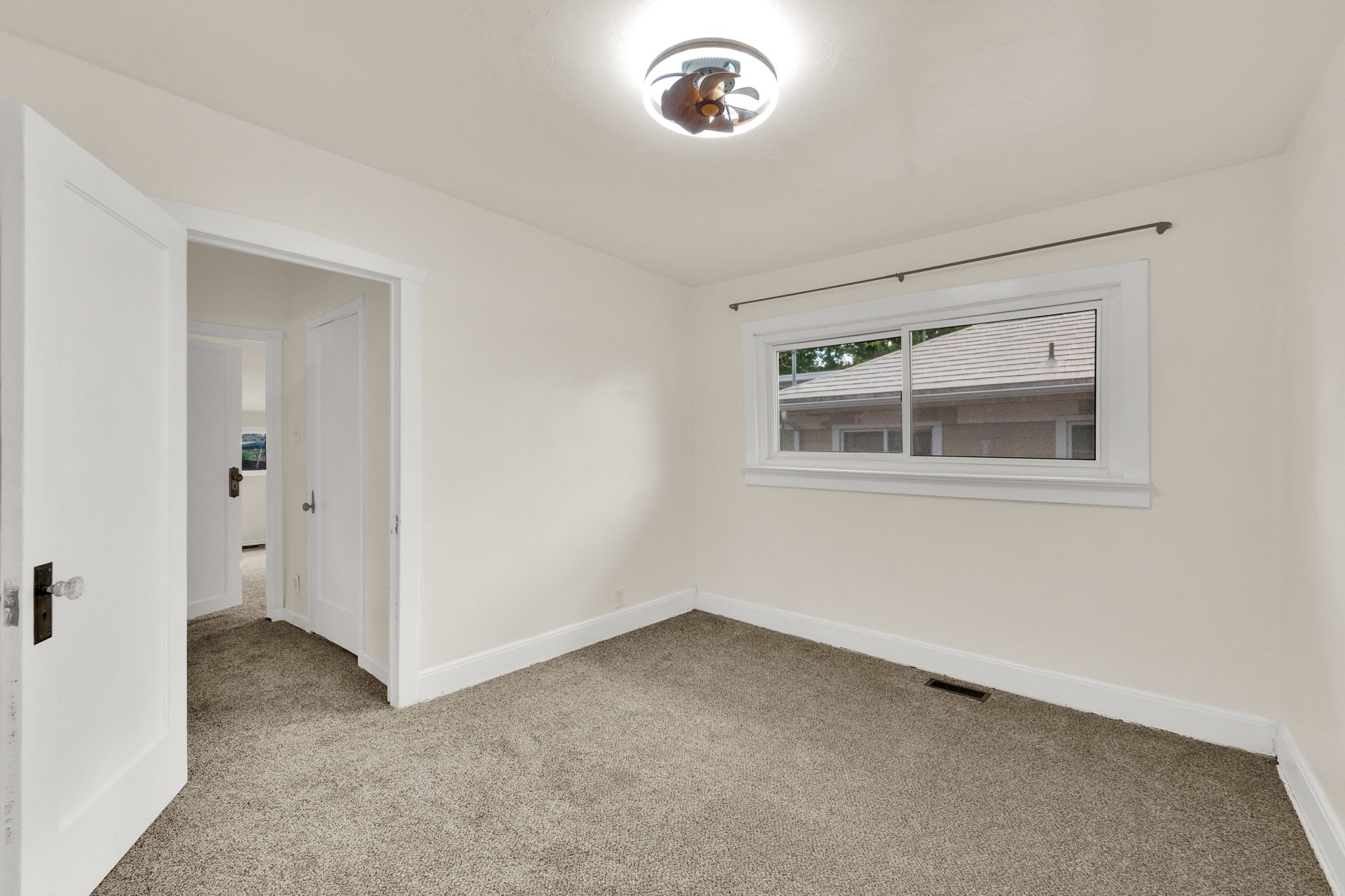 Neutral tone wall paint, light-colored carpet flooring, white trim, single window, and a ceiling light fixture