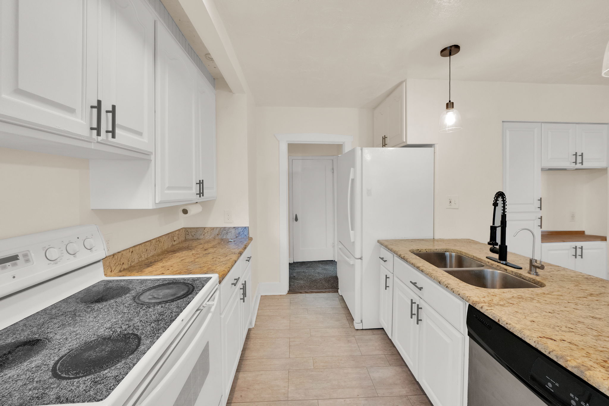 Kitchen featuring white cabinetry with dark hardware, granite-style countertops, stainless steel double basin sink with a matte black faucet, and tile flooring