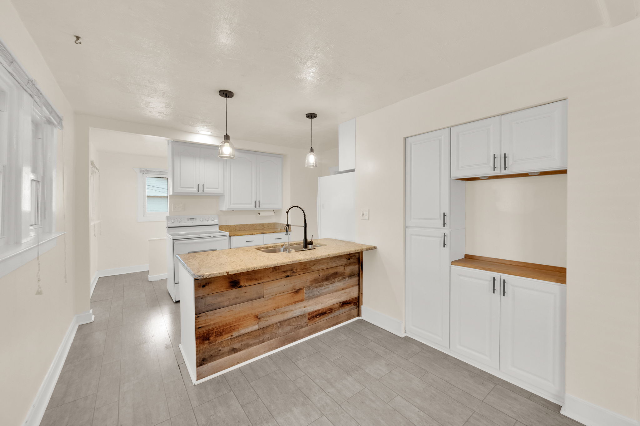 Kitchen featuring a wood-finish island with a stone countertop and integrated sink, white shaker-style cabinetry, a white electric range, and wood-finish flooring