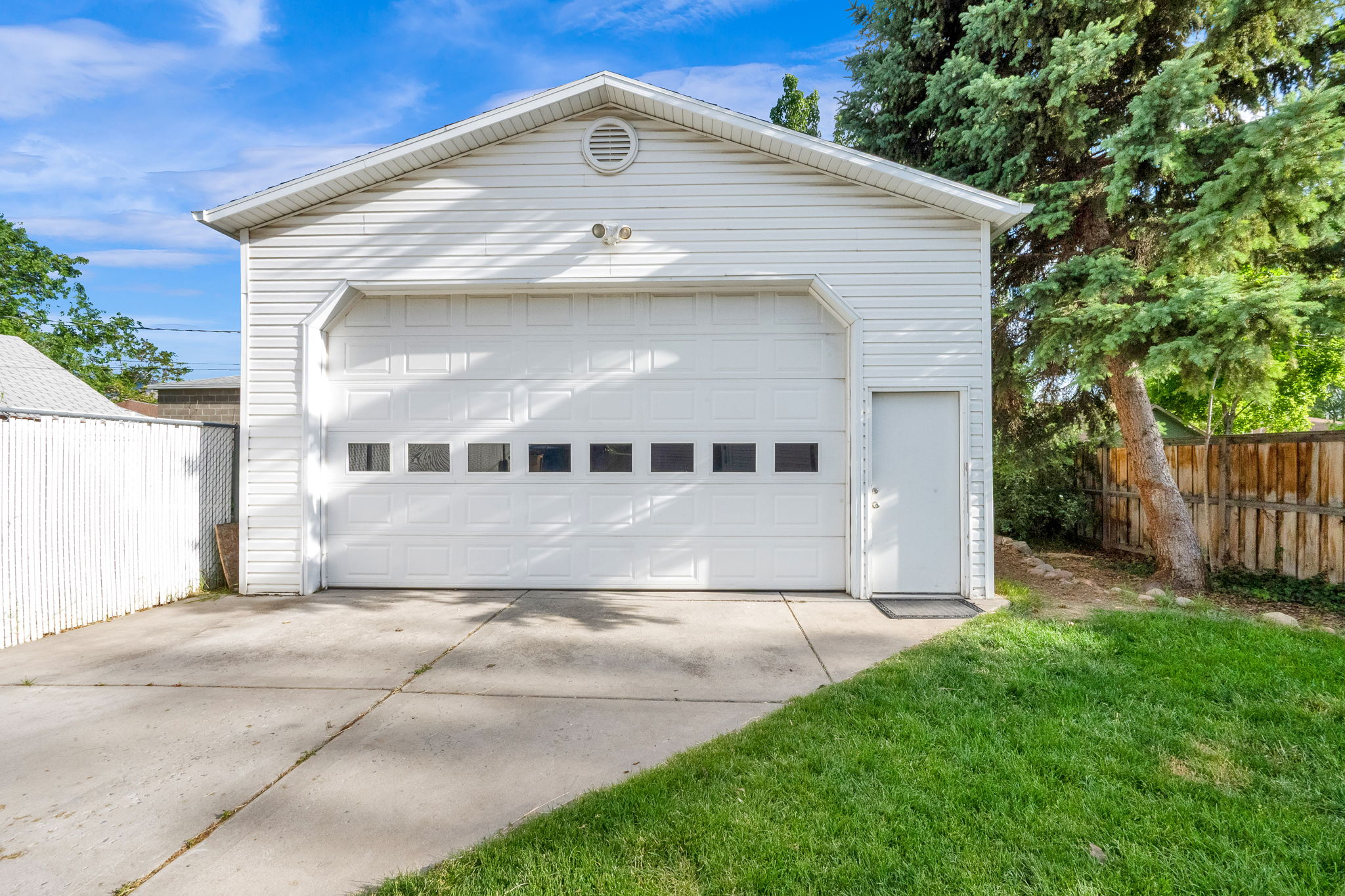 Detached garage with white vinyl siding and a single overhead door featuring transom-style windows