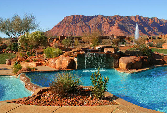 Swimming pool with rock waterfall feature, integrated spa, and surrounding desert landscaping